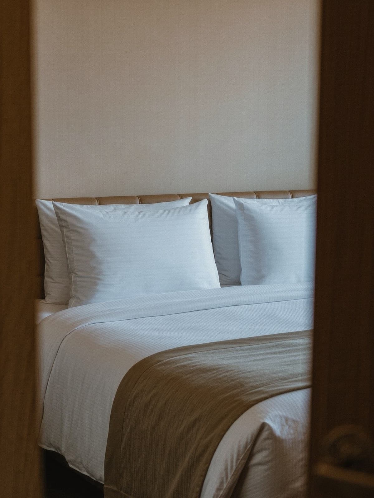 Bembeyaz takımlarla hazırlanmış otel yatağı; ayak ucunda katlı şal, başucunda iki kırlent